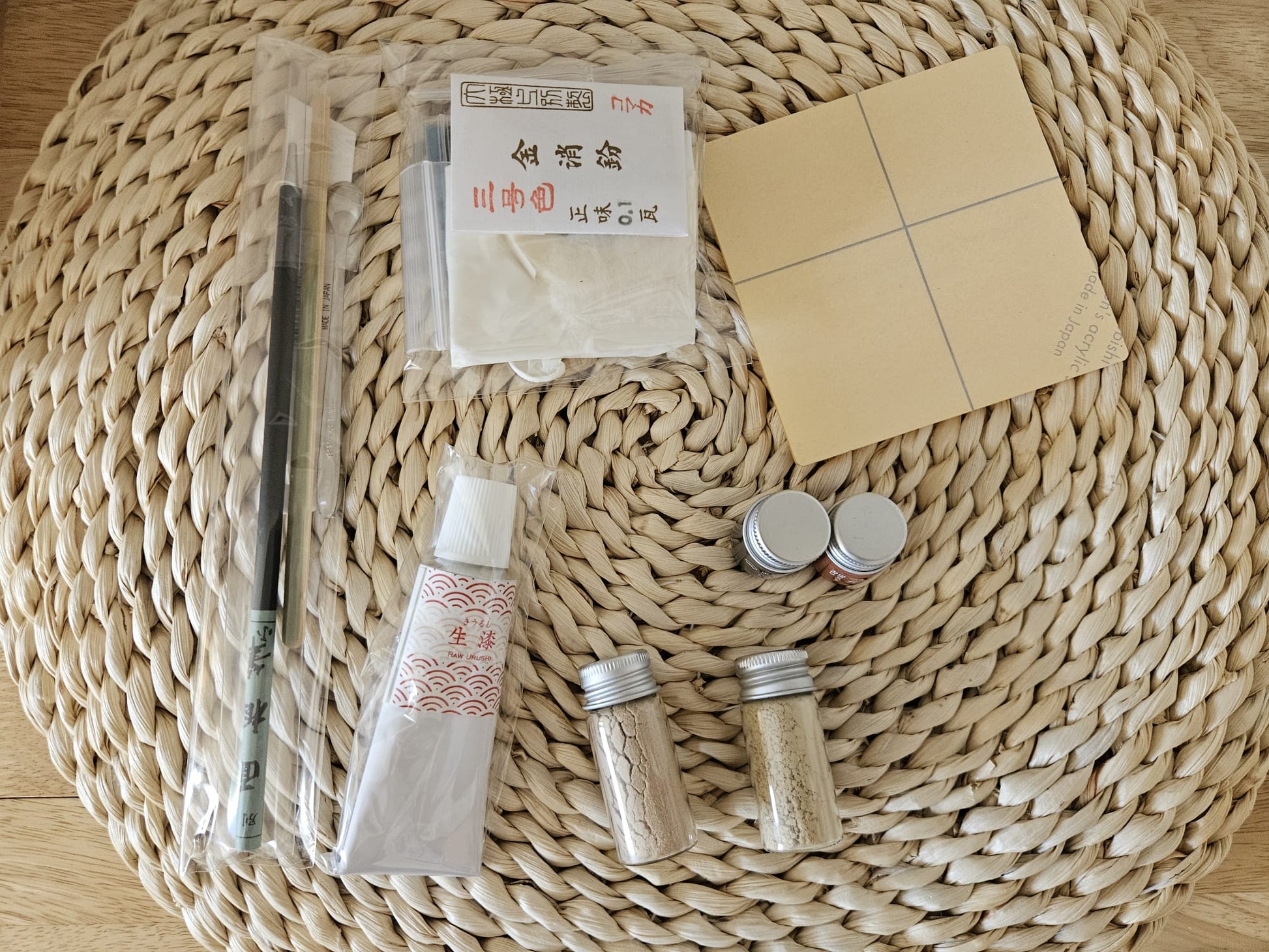 Kitntsugi kit set for beginners featuring a sand paper, ink, palette dropper, spatula, gold powder, masking tape on a woven background.